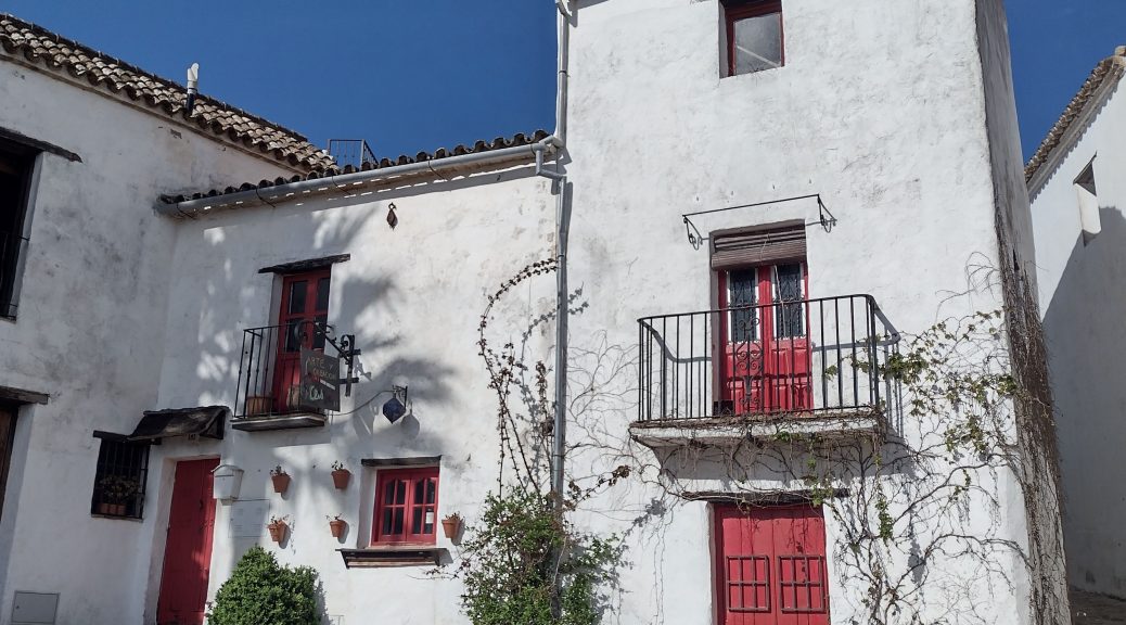 A whitewashed house in Castellar de la Frontera with red doors and window frames and a sherry barrel outside