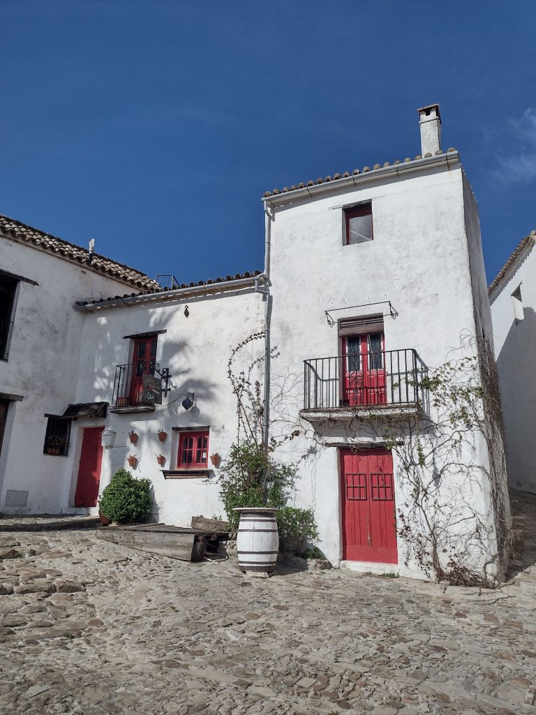 A whitewashed house in Castellar de la Frontera with red doors and window frames and a sherry barrel outside